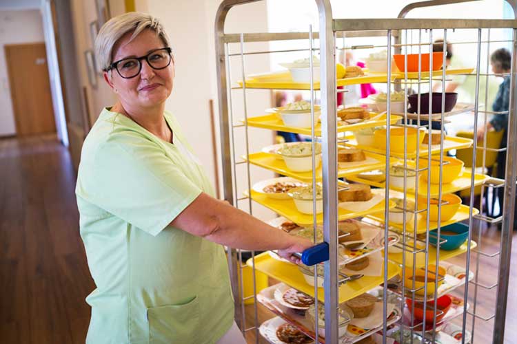 facility staff member pulling tray of food