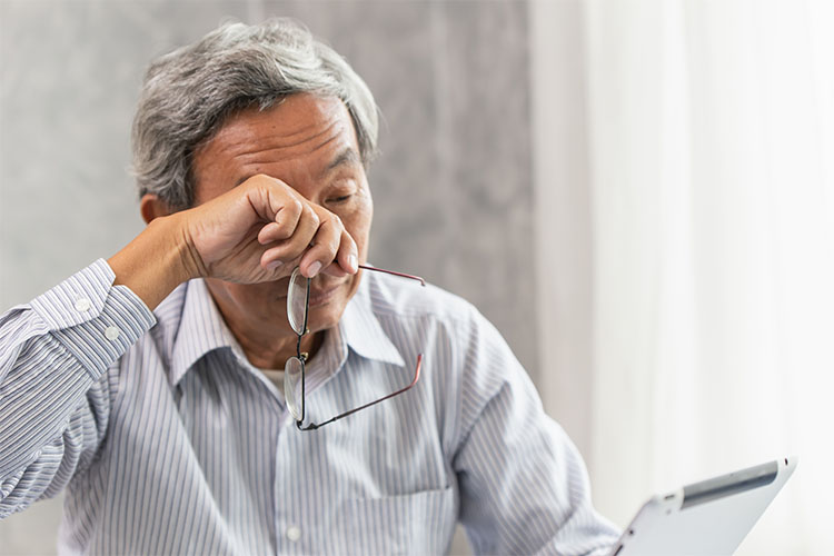 older man holding glasses and wiping eyes while looking at tablet device